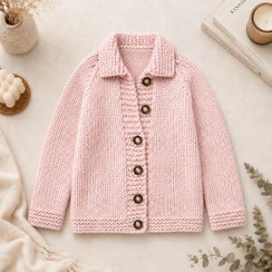 May include: A light pink long-sleeve knit cardigan featuring a collared neckline and a front button closure with six dark brown buttons. The garment is constructed with a chunky knit texture, ribbed cuffs, and a ribbed hemline along the bottom edge.