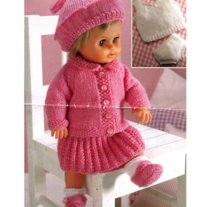 May include: A doll dressed in a pink knitted ensemble: a jacket, skirt, hat, and booties. The jacket fastens with buttons. A smaller white knitted top and shorts are visible. The doll is seated on a white chair.