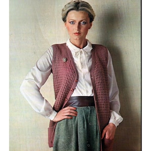 May include: A woman in a vintage outfit. The outfit features a mauve knitted vest with a button-up front, a white blouse with a bow, a green skirt, and a brown belt. A small brooch is pinned to the vest.
