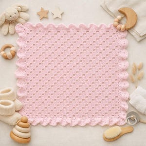 May include: A soft pink crochet baby blanket with a scalloped edge. The blanket is surrounded by baby items, including a stuffed bunny, wooden toys, baby booties, and a hairbrush. The blanket measures approximately 30 inches square.