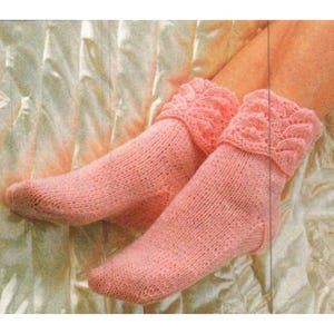 Op de afbeelding: Een paar lichtroze gebreide sokken met een decoratieve, patroonboord. De sokken zijn gemaakt van zacht, getextureerd garen en lijken handgemaakt. De boord toont een ingewikkeld patroon.