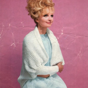 May include: A vintage photograph features a woman wearing a light blue dress and a white knitted shawl. The shawl has a textured pattern and covers the shoulders and arms. The woman has blonde hair and is smiling. The background is a pink color.