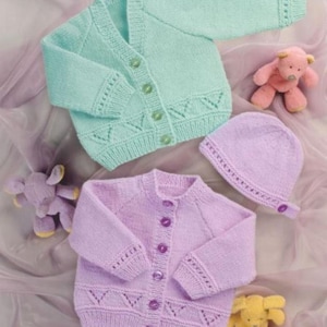 Op de afbeelding: Twee gebreide babyvesten, één lichtblauw en één lavendelkleurig, met bijpassende knopen en decoratieve stiksels. Er is ook een lavendelkleurige gebreide baby muts aanwezig. De kledingstukken worden gepresenteerd met twee knuffels op een zachte, roze achtergrond.