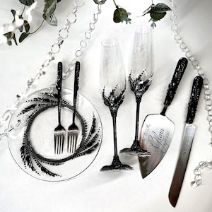 May include: Elegant wedding set featuring two champagne flutes, a cake server, and a knife. The set includes a plate and two forks. All items have black decorative accents. The cake server and knife are engraved with names and a date.