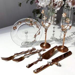 May include: A luxurious wedding or celebration serving set. Includes two champagne flutes, a cake stand, cake server, knife, and two forks. All pieces are decorated with gold-tone metal and crystal embellishments.