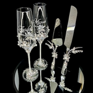 Silver jeweled wedding flutes and cake cutting set arranged on a glamorous reception head table.