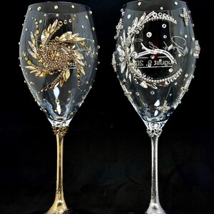 Könnte beinhalten: Zwei Weingläser aus klarem Glas, verziert mit Strasssteinen. Das linke Glas hat einen goldenen Stiel und Fuß mit einem goldenen Blumenmuster aus Strass. Das rechte Glas hat einen silbernen Stiel und Fuß mit einem silbernen Mondsichel-Design.
