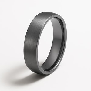 Puede incluir: Un anillo gris oscuro con un acabado de metal cepillado. El anillo tiene un perfil redondeado y un interior liso y oscuro. El anillo es un diseño simple y elegante, adecuado para el uso diario.