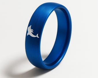 May include: A vibrant blue ring with a brushed metal finish. A white dolphin silhouette is etched on the ring's surface. The ring is a solid band, showcasing a sleek and modern design.