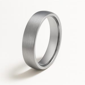 May include: A brushed silver ring with a flat profile. The ring has a smooth, matte finish and a simple, elegant design. The ring is likely made of a durable metal, such as stainless steel or titanium.