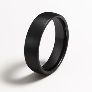 May include: A black ring with a brushed metal finish. The ring has a smooth, rounded interior and a flat, textured exterior. The ring is set against a white background, with a shadow cast to the side.