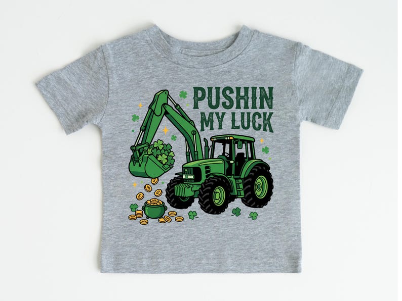 May include: A gray t-shirt featuring a green tractor with a bucket full of shamrocks and gold coins. The text "PUSHIN MY LUCK" is printed above the tractor. The design is a St. Patrick's Day theme.