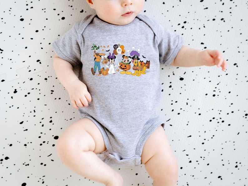 May include: A gray baby onesie featuring a colorful Halloween-themed graphic. The graphic includes cartoon characters dressed in costumes, such as a ghost, a pirate, and a pumpkin. The onesie is short-sleeved and has a simple, classic design.