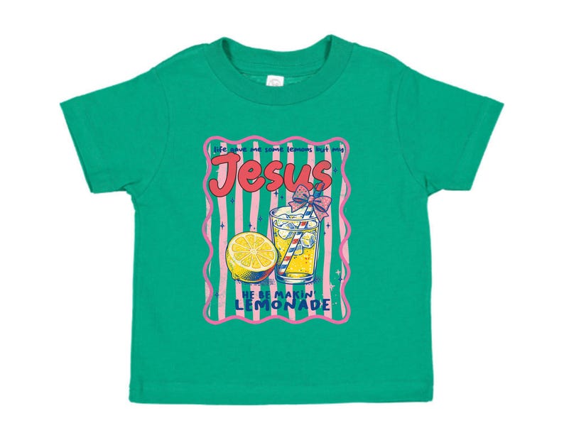 May include: A green toddler t-shirt with a graphic design. The design features the word "Jesus" in pink, a glass of lemonade, and a lemon slice. The text "Life gave me lemons but God" and "He be makin lemonade" are also included.