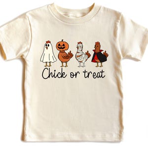 Peut inclure: T-shirt crème avec un motif sur le thème d'Halloween. Le dessin comprend quatre poulets de dessin animé déguisés en fantôme, citrouille, momie et vampire, avec le texte "Chick or treat" en dessous.