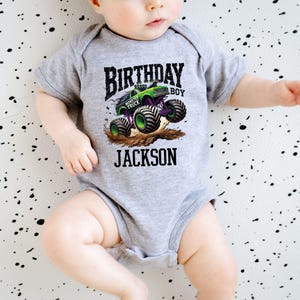 Pode incluir: Um body cinza para beb&eacute; com um gr&aacute;fico de monster truck. O design apresenta um monster truck verde e preto com rodas roxas, as palavras "BIRTHDAY BOY" e o nome "JACKSON".