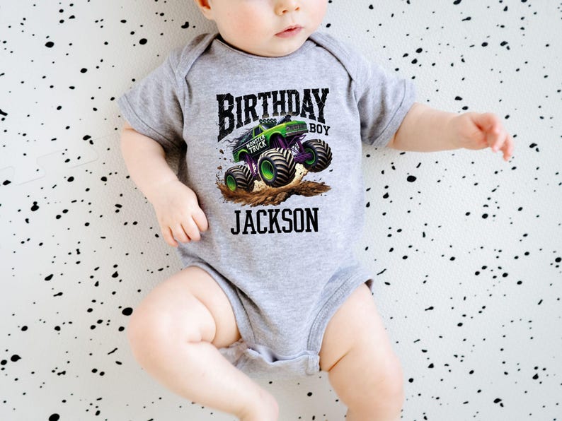 Pode incluir: Um body cinza para beb&eacute; com um gr&aacute;fico de monster truck. O design apresenta um monster truck verde e preto com rodas roxas, as palavras "BIRTHDAY BOY" e o nome "JACKSON".