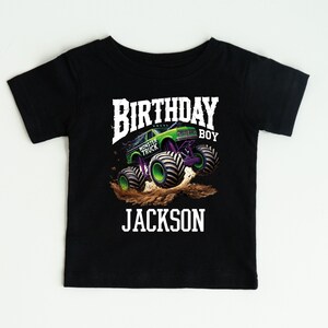 Pode incluir: Camiseta preta de manga curta com um gr&aacute;fico de monster truck. O design inclui as palavras "BIRTHDAY BOY" e "JACKSON" em branco, com uma imagem de monster truck verde e roxo.