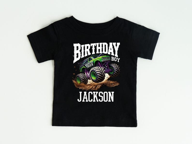 Pode incluir: Camiseta preta de manga curta com um gr&aacute;fico de monster truck. O design inclui as palavras "BIRTHDAY BOY" e "JACKSON" em branco, com uma imagem de monster truck verde e roxo.
