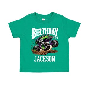 Pode incluir: Uma camiseta verde com um gr&aacute;fico de um monster truck e o texto "BIRTHDAY BOY JACKSON". O monster truck &eacute; verde e preto com rodas roxas, levantando terra.