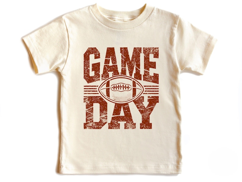 K&ouml;nnte beinhalten: Cremefarbenes Kurzarm-T-Shirt mit einem braunen Used-Look-Grafik. Die Grafik zeigt "GAME DAY" &uuml;ber und unter einer Football-Illustration. Das Shirt besteht aus einem weichen, bequemen Material.