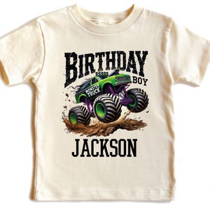 Pode incluir: Camiseta creme com um design de monster truck verde e roxo. O texto "BIRTHDAY BOY MONSTER TRUCK JACKSON" &eacute; impresso acima e abaixo do gr&aacute;fico do caminh&atilde;o. O design inclui respingos de lama.