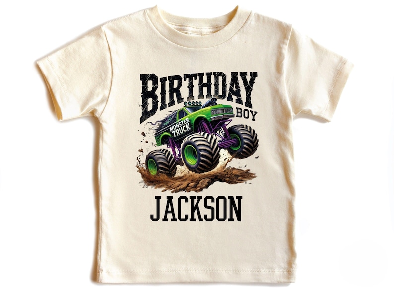 Pode incluir: Camiseta creme com um design de monster truck verde e roxo. O texto "BIRTHDAY BOY MONSTER TRUCK JACKSON" &eacute; impresso acima e abaixo do gr&aacute;fico do caminh&atilde;o. O design inclui respingos de lama.