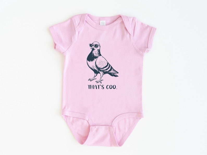 May include: A light pink baby bodysuit with a black graphic of a pigeon wearing sunglasses. The text "THAT'S COO." is printed below the bird. The bodysuit is made of soft material.