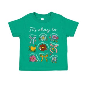 May include: A green toddler t-shirt with the phrase "It's okay to..." and various floral and bow graphics. The shirt features text such as "Start over", "Make mistakes", and "Have a bad day".