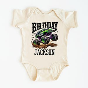 Pode incluir: Um body de beb&ecirc; bege com um gr&aacute;fico de monster truck verde e roxo. O texto diz "BIRTHDAY BOY" acima do caminh&atilde;o e "JACKSON" abaixo. O design apresenta um monster truck levantando poeira.