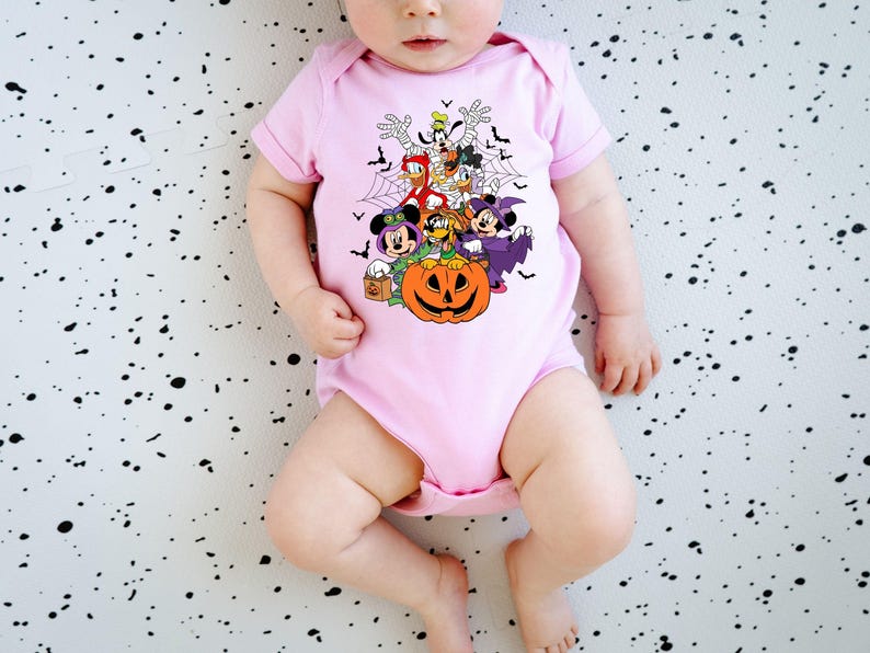 Op de afbeelding: Lichtroze babybody met een Halloween-thema. De afbeelding toont Mickey Mouse, Minnie Mouse, Donald Duck en Goofy in Halloween-kostuums, een pompoen en vleermuizen.