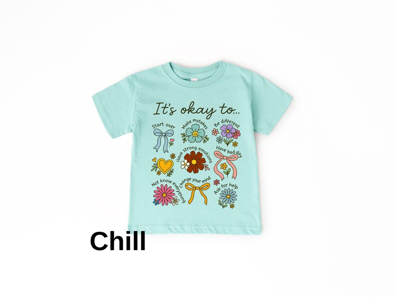 May include: A light blue t-shirt with the text "It's okay to..." and various floral and bow graphics. The shirt also has the word "Chill" printed at the bottom in black.