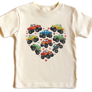 May include: Cream-colored t-shirt featuring a heart-shaped arrangement of colorful monster trucks. Each truck has a unique design and color, with small red hearts scattered around the trucks. The shirt is made of soft material.