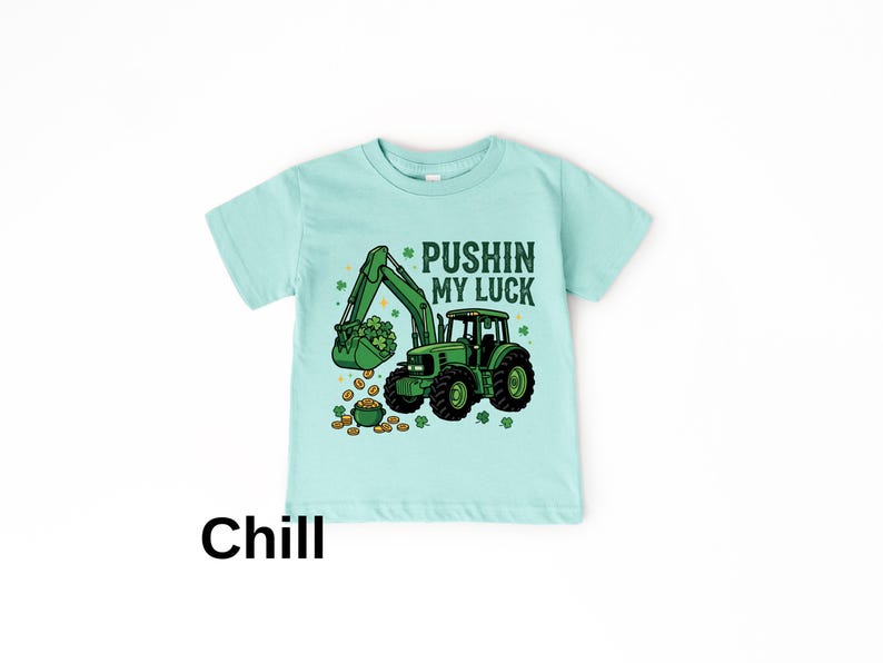 May include: A light blue t-shirt featuring a green tractor with a bucket full of shamrocks and gold coins. The text "Pushin' My Luck" is above the tractor. The word "Chill" is at the bottom.
