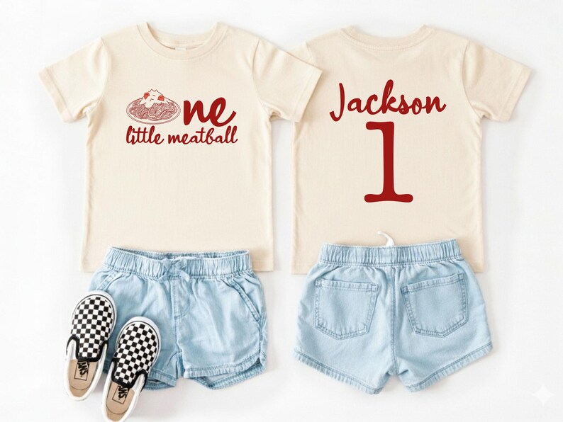 May include: A cream-colored toddler outfit featuring a t-shirt with a red graphic of spaghetti and the words "one little meatball." The back of the shirt has the name "Jackson" and the number "1" in red. Includes denim shorts and checkered sneakers.