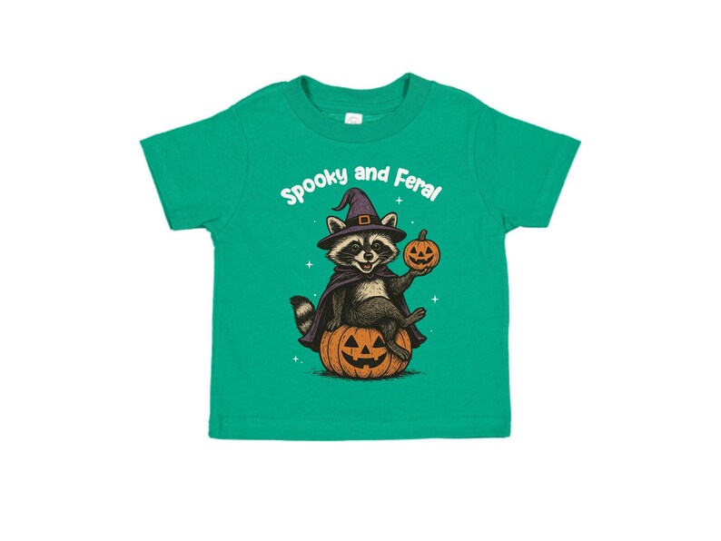 Peut inclure: T-shirt vert pour enfant avec un motif d'Halloween. Il repr&eacute;sente un raton laveur portant un chapeau et une cape de sorci&egrave;re, assis sur une citrouille sculpt&eacute;e et tenant une lanterne. Le texte "Spooky and Feral" est au-dessus du raton laveur.