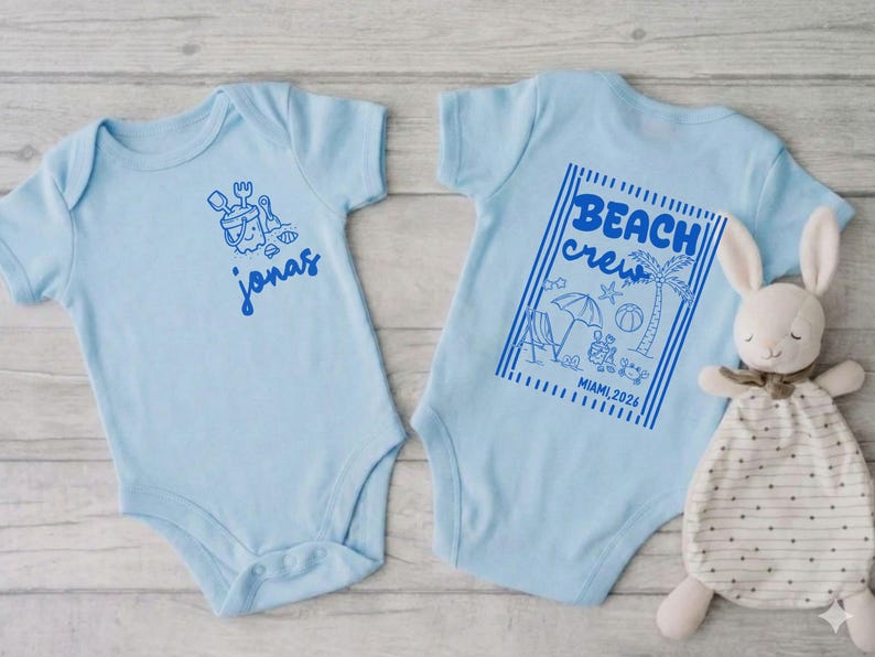 Op de afbeelding: Lichtblauwe babybody met een strandthema. E&eacute;n body heeft de naam "Jonas" in blauw. De andere heeft een "Beach Crew" ontwerp met een palmboom, parasol en de tekst "Miami 2024". Een knuffelkonijn ligt naast de body.