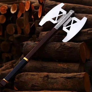 May include: A double-bladed axe with a silver head and a dark brown wooden handle. The handle has a black grip with gold accents. The axe is resting on a pile of wooden logs, suggesting a tool for chopping wood.