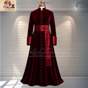 Puede incluir: Un vestido largo de terciopelo burdeos con cuello alto y mangas largas. El vestido presenta una fila de botones en la parte delantera y una faja de satén a juego. Los puños y la faja son de un tono burdeos ligeramente más brillante. El vestido se exhibe en un maniquí.
