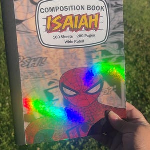 May include: Composition book featuring a Spiderman design with the name "Isaiah" in a bold, yellow and red font. The cover includes the text "100 Sheets, 200 Pages, Wide Ruled". The notebook has a black spine.