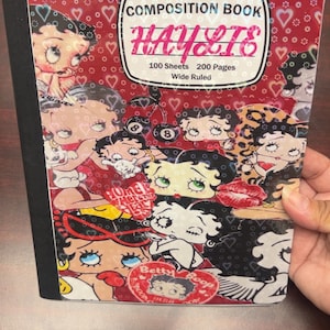 Könnte beinhalten: Ein Collegeblock mit breiter Linierung mit einer Collage von Betty-Boop-Illustrationen auf rotem Hintergrund mit Herzakzenten. Der Einband enthält den Text "HAYLIE'S" und "COMPOSITION BOOK". Das Buch hat 100 Blatt und 200 Seiten.