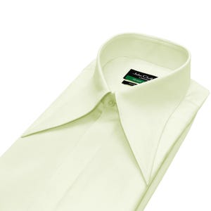 Puede incluir: Una camisa amarillo pálido con un cuello ancho. La camisa está cuidadosamente doblada y tiene un cuello abotonado. La etiqueta dice "John Cloth London".
