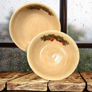 May include: Two beige ceramic bowls with a pine cone and evergreen design. The bowls are stacked on top of each other.
