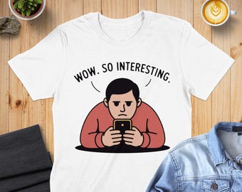 May include: White t-shirt with the phrase "WOW. SO INTERESTING." above a cartoon illustration of a person looking at a phone with a bored expression. The person is wearing a red shirt.
