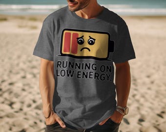May include: A gray t-shirt with the text "RUNNING ON LOW ENERGY." The shirt features a cartoon battery graphic with a sad face, indicating low power. The design is printed in black and yellow.