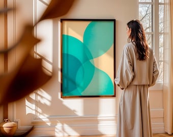 May include: A framed abstract art print with overlapping teal and turquoise shapes on a beige background. The artwork is displayed on a white wall. A person is standing in front of the artwork.