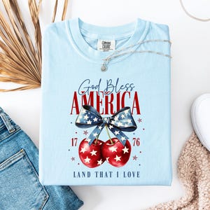 Camiseta americana con cerezas en colores cómodos, camiseta del 4 de julio con cerezas, camiseta del Día de los Caídos con cerezas, camiseta con lazo patriótico, camiseta americana.