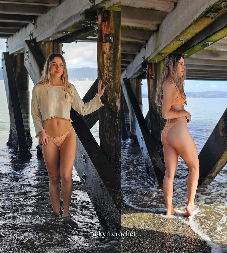 Puede incluir: Conjunto de bikini de crochet en color melocot&oacute;n claro. El conjunto incluye un top corto de manga larga y una braguita de estilo tanga. La imagen est&aacute; tomada al aire libre bajo un muelle de madera. El texto "@kyn.crochet" es visible.