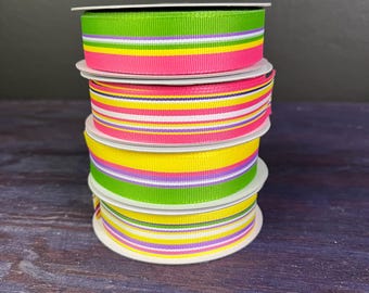 May include: Four spools of striped ribbon in a stack. The ribbon is yellow, pink, green, and purple.