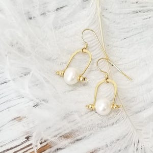 May include: Gold hoop earrings with a white pearl and small gold beads hanging from the bottom.